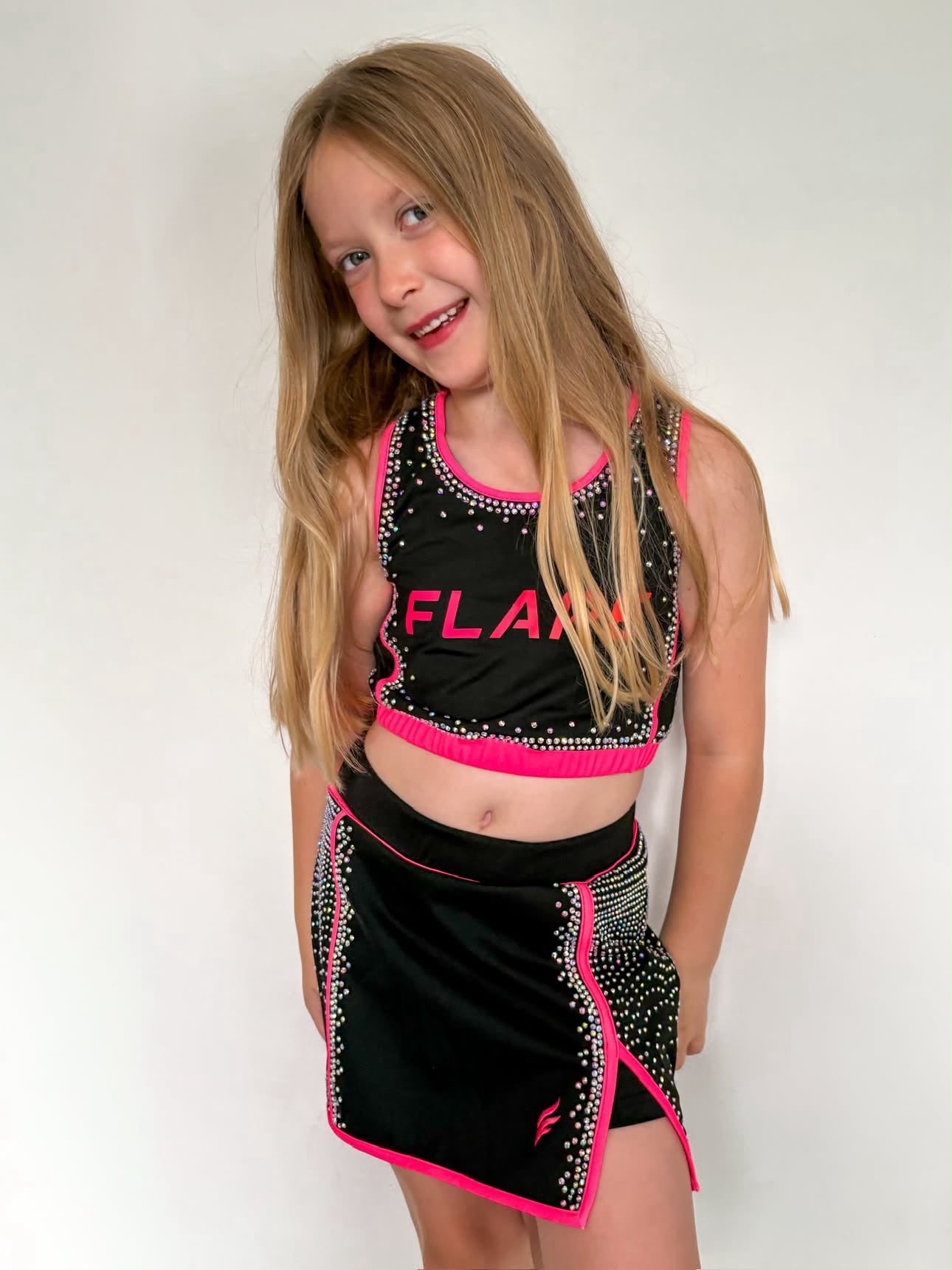 Young cheerleader wearing a black and pink rhinestone Flare crop top and skort set